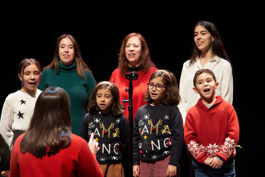Crianças e adultos de camisola de Natal a cantar juntos em palco no Recital de Natal 2024