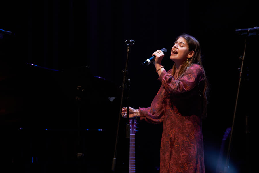 Aluna adulta a cantar ao microfone, luz azul de palco