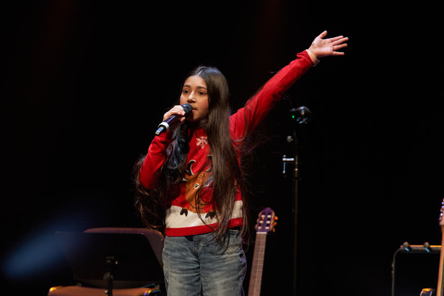 Aluna a cantar com o braço no ar, camisola vermelha de Natal